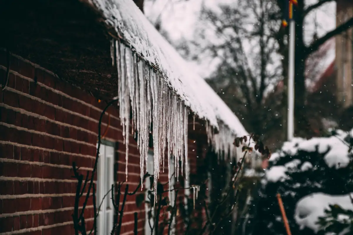 Icicles hanging the length of a brick house's eave under a roof still loaded with snow